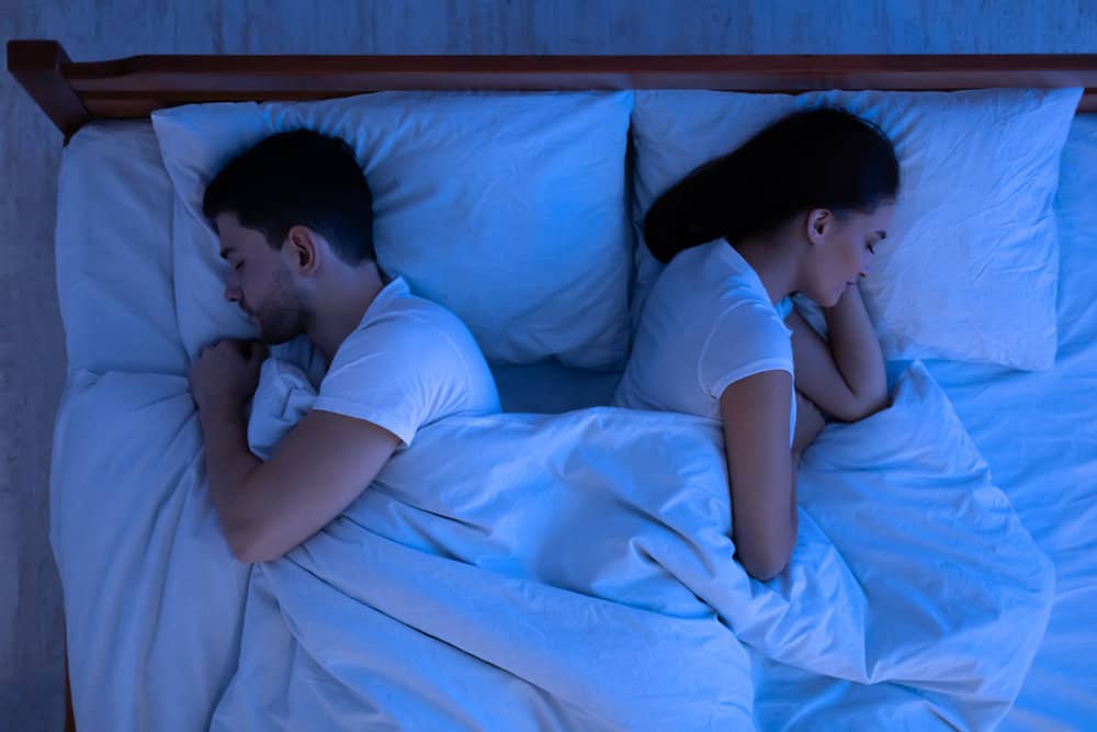 Spouses sleeping lying back-to-back in bed in bedroom, above view