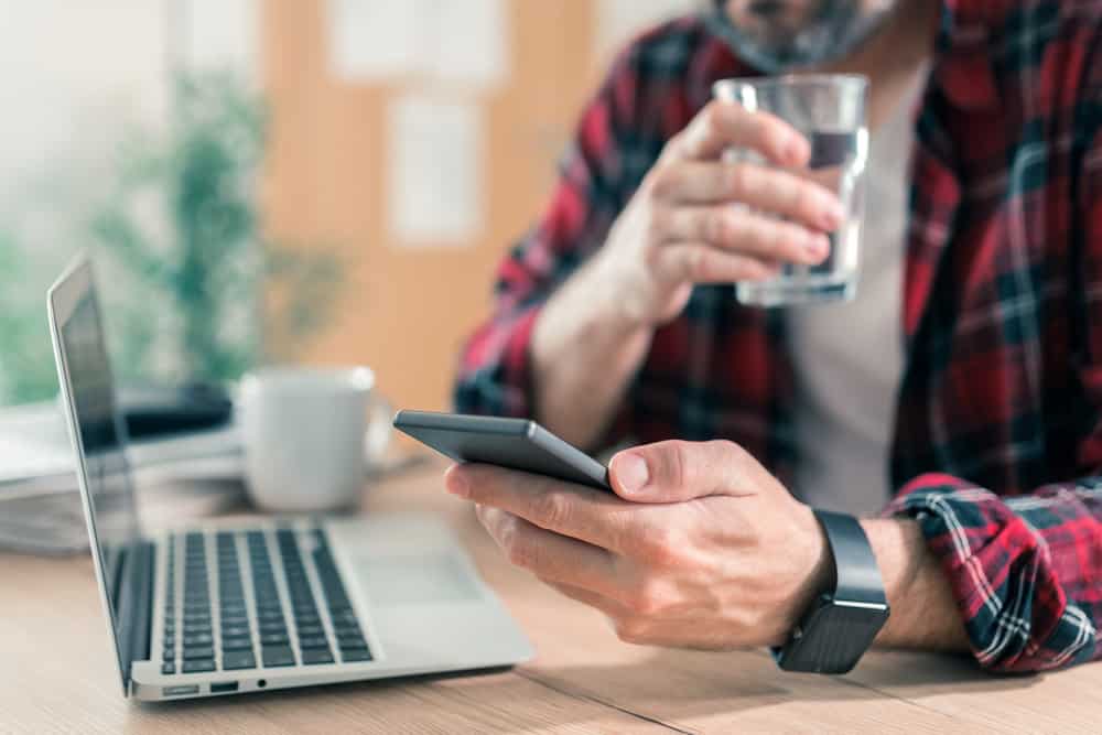 Man drinking water and using mobile phone in home office