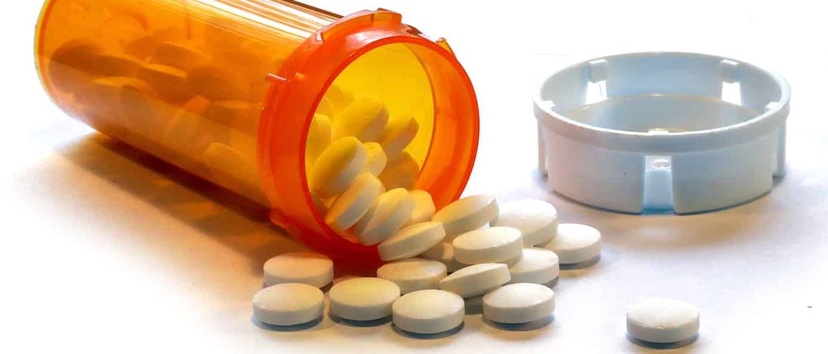 Prescription pill bottle tipped over with white tablets spilling out