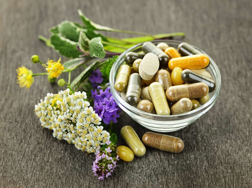 Herbal supplement capsules in a bowl next to fresh herbs
