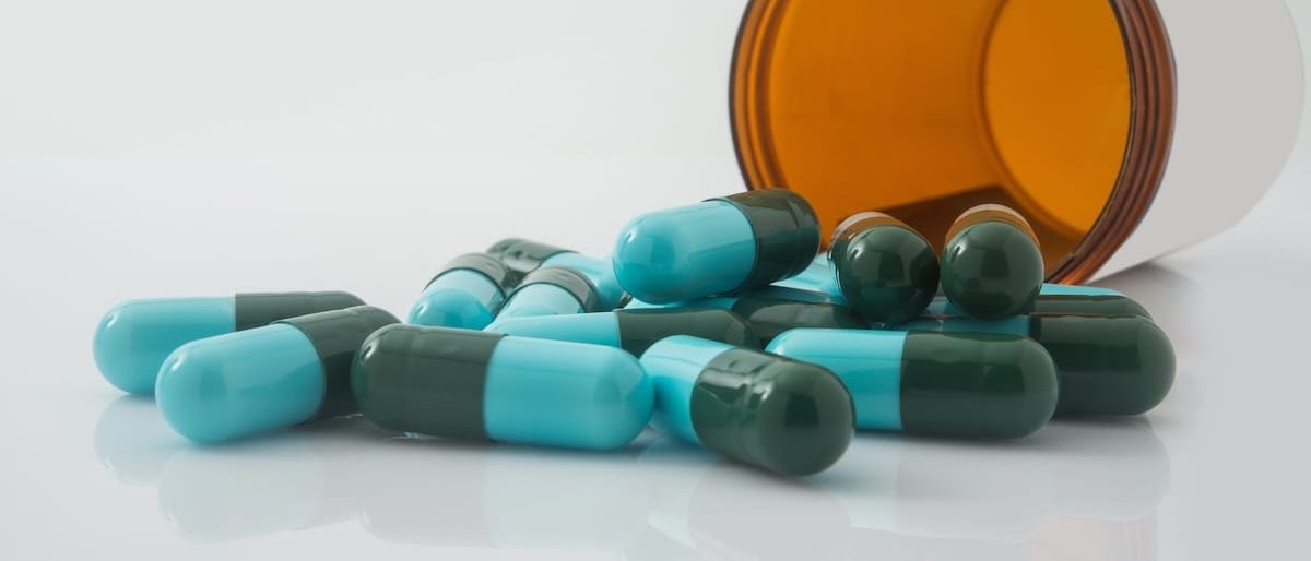 Green and blue capsules spilling from an amber supplement bottle
